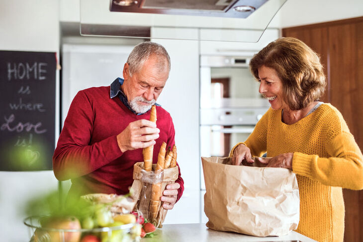 kobieta i mężczyzna w kuchni rozpakowują zakupy z papierowej torby