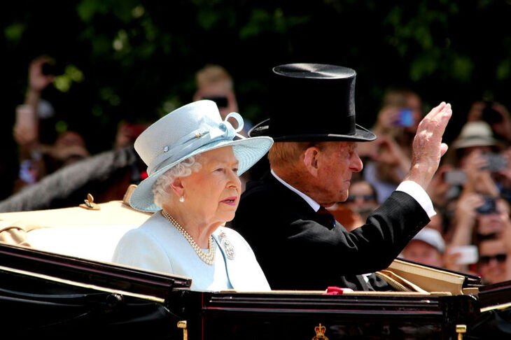 Królowa Elżbieta II w białym stroju siedząca w powozie