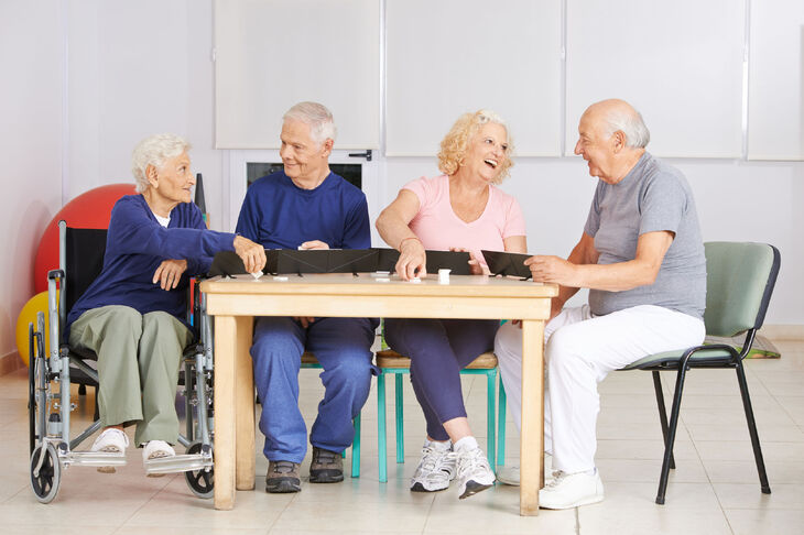 Seniorzy przy stolę grają w grę towarzyską 