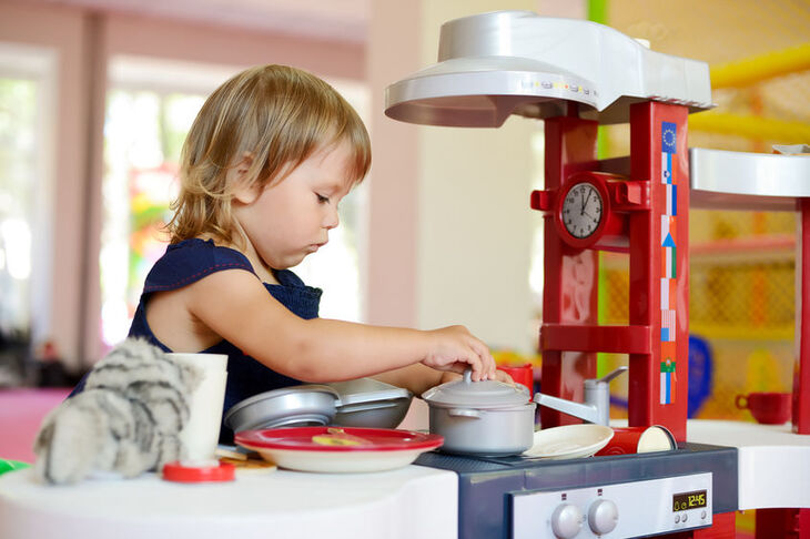 Trzyletnia dziewczynka bawi się zabawkową kuchnią
