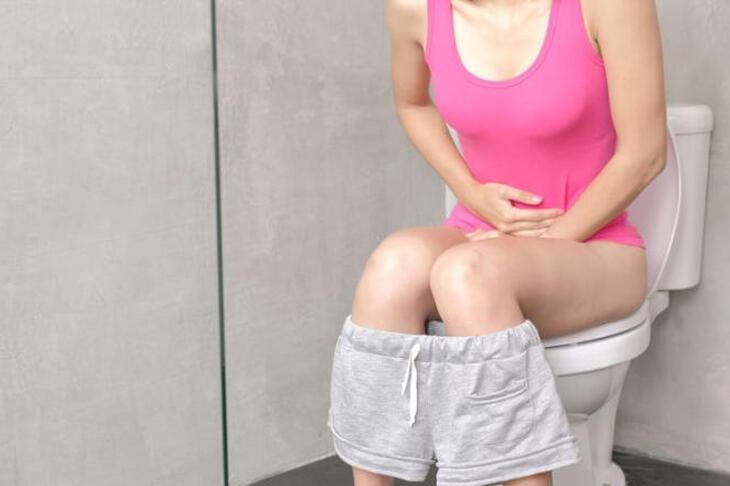 Kobieta siedząca na toalecie trzymająca się za brzuch