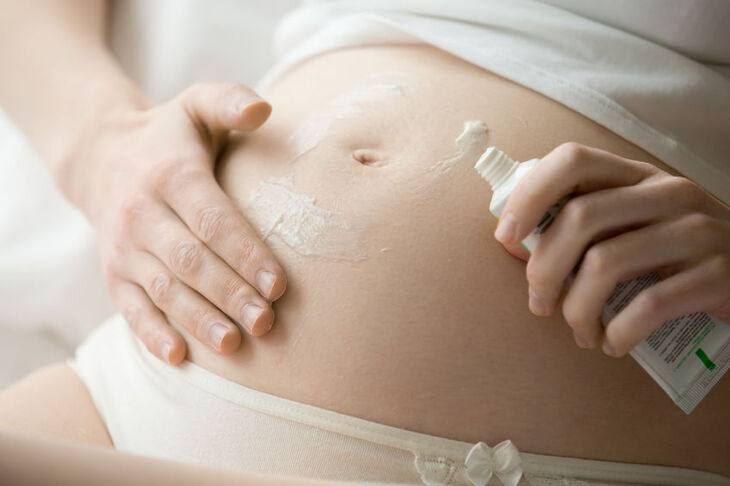 Kobieta w ciąży wciera w brzuch balsam na rozstępy