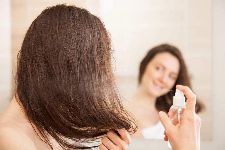 Kobieta spryskuje włosy odżywką bez spłukiwania