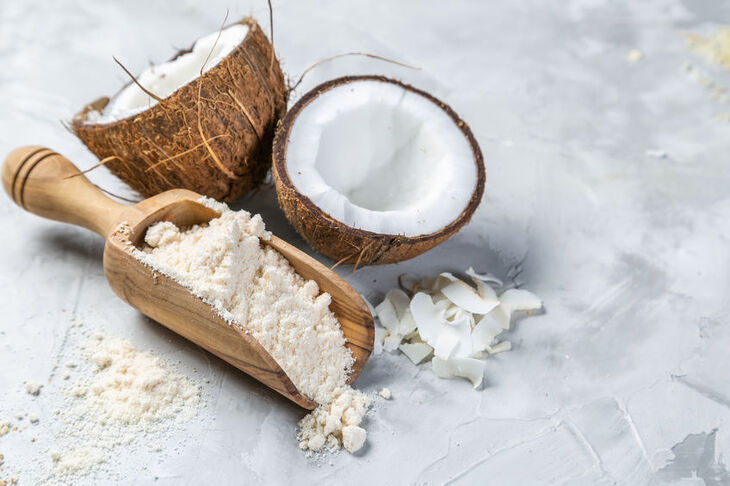 Mąka kokosowa na drewnianej łyżce i przepołowiony kokos