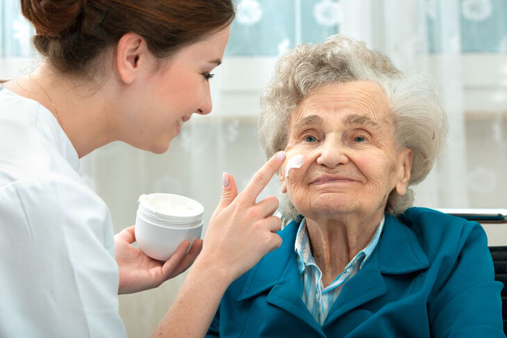 Lekarz smaruje twarz starszej kobiety kremem 