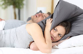 Mężczyzna chrapie, a kobieta chowa głowę pod poduszką