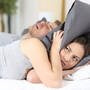Mężczyzna chrapie, a kobieta chowa głowę pod poduszką