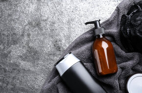 srebrna i brązowa butelka kosmetyku na szarym ręczniku i kamiennym tle - całość budzi skojarzenia z produktami do siwych włosów