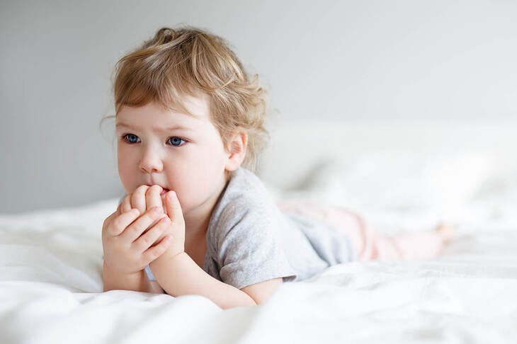Dziecko obgryzające paznokcie w trakcie leżenia na łóżku