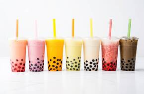 6 bubble tea w typowych przezroczystych plastikowych kubkach ustawione w rzędzie. Każda w innym kolorze i o innym smaku. 