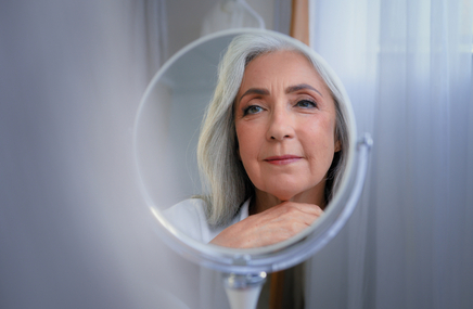 Kobieta w średnim wieku w okresie menopauzy przygląda się w lusterku