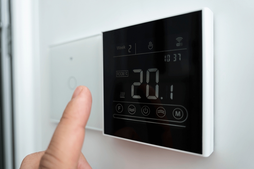 Zbliżenie męskiej dłoni regulującej nowoczesny cyfrowy termostat montowany na ścianie. Na wyświetlaczu temperatura 20 stopni celsjusza.