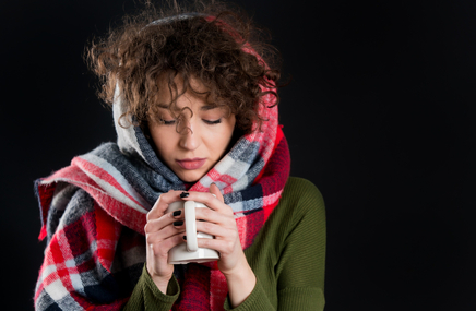 Zmarznięta kobieta, chora na grypę ogrzewa dłonie kubkiem gorącej herbaty