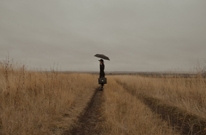 Samotna kobieta z parasolem i teczką na drodze polnej