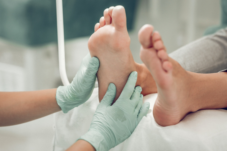 Lekarz w zielonych rękawiczkach jednorazowych bada stopę cukrzycową pacjenta