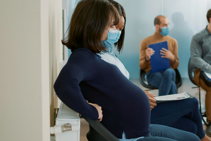 Kobieta w maseczce czeka w poczekalni do lekarza i przechodzi covid w ciąży