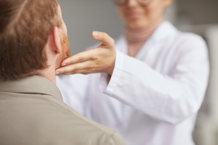 Lekarka bada mężczyznę pod kątem nowotworów głowy i szyi