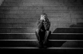 Mężczyzna z depresją siedzi na schodach i zakrywa twarz dłońmi