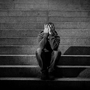 Mężczyzna z depresją siedzi na schodach i zakrywa twarz dłońmi