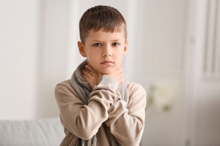 Dziecko trzymające się za gardło, możliwe objawy anginy wirusowej