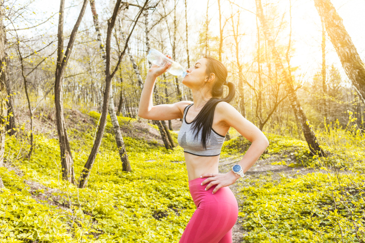 Wysportowana kobieta piję wodę w trakcie biegania