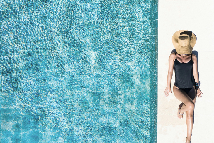 Atrakcyjna kobieta opala się nad basenem w jednoczęściowym stroju kąpielowym