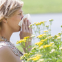 Kobieta wśród żółtych kwiatów wyciera nos chusteczką, bo ma alergię na pyłki