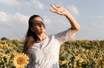 Kobieta z alergią na słońce pośród słoneczników zasłania się ręką