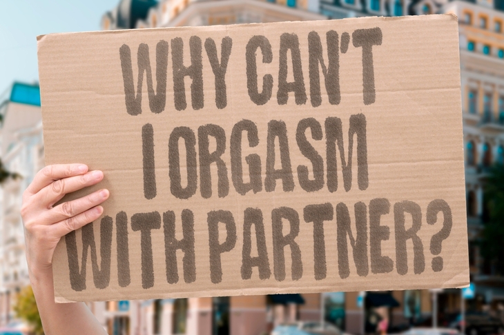 Osoba trzymająca kartonowy transparent z napisem „Why can't I orgasm with partner?” (Dlaczego nie mogę osiągnąć orgazmu z partnerem?)