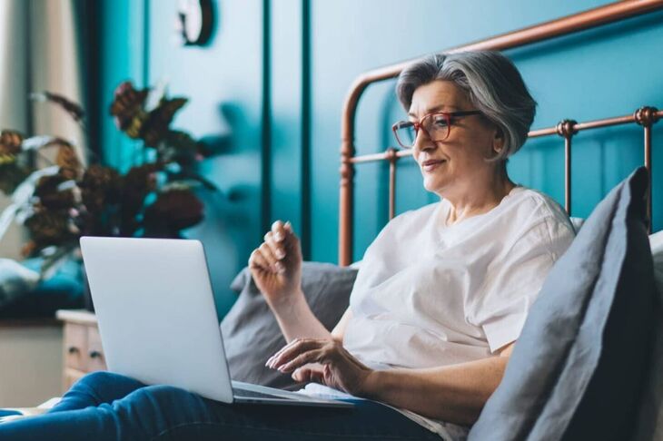 seniorka leżąca w łóżku i pracująca na laptopie