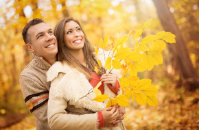 Mężczyzna przytulający kobietę w parku i trzymający jesienne liście