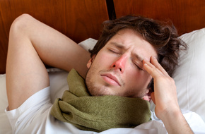 Mężczyzna z zaczerwienionym nosem i szalkiem na szyi leżący w łóżku
