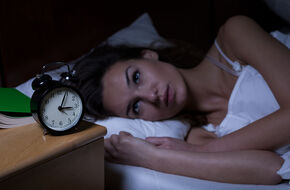 Kobieta leżąca nocą na łóżku i patrząca na zegarek