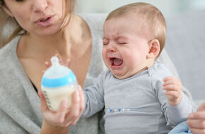 Płaczące niemowlę trzymające butelkę z mlekiem