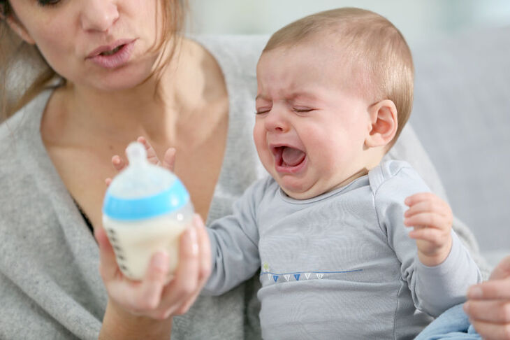 Płaczące niemowlę trzymające butelkę z mlekiem
