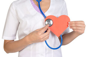 Pielęgniarka w białym fartuchu trzymająca w dłoni papierowe serce i stetoskop