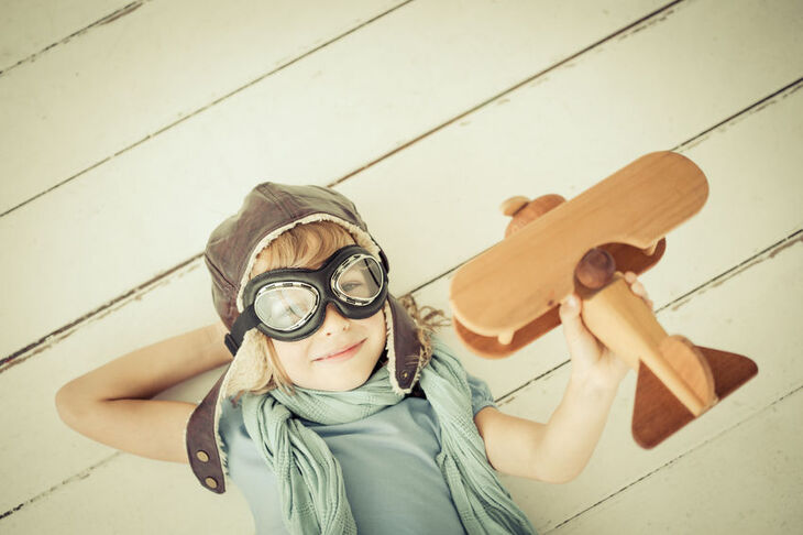 Chłopczyk w czapce pilota z drewnianym samolotem w dłoni