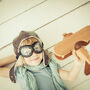 Chłopczyk w czapce pilota z drewnianym samolotem w dłoni