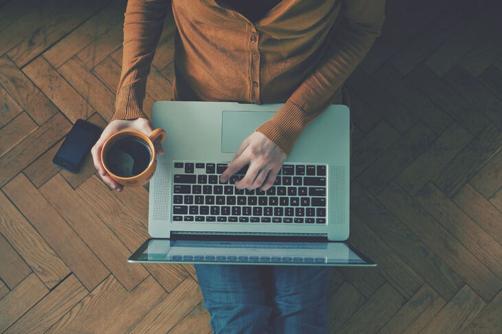 Osoba siedząca przy laptopie z kubkiem kawy