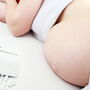 Kobieta w zaawansowanej ciąży leżąca na łóżku z termometrem i tabletkami