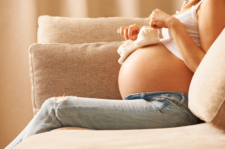 Kobieta w zaawansowanej ciąży trzymająca na brzuchu buciki