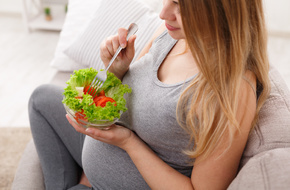 Kobieta w zaawansowanej ciąży jedząca sałatkę z miski